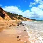 Praia do Litoral Norte com águas cristalinas. Falésias coloridas e céu azul com nuvens. Paraíso tropical.